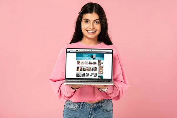 QUIIV, UCRÂNIA - JULHO 30, 2019: menina sorridente segurando laptop com site da amazônia na tela, isolado em rosa — Fotografia de Stock