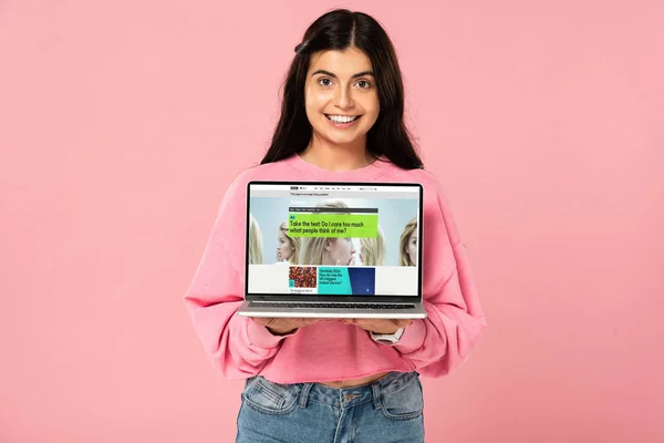 KYIV, UKRAINE - JULY 30, 2019: smiling girl holding laptop with BBC website on screen, isolated on pink — Stock Photo