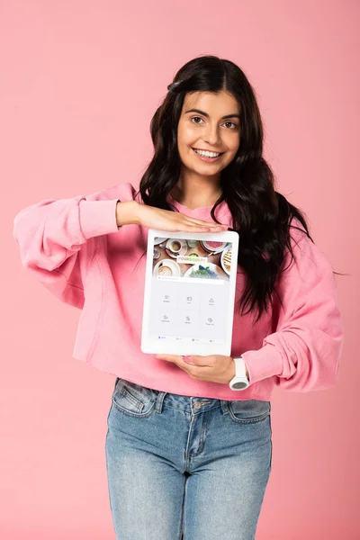 KYIV, UCRAINA - 30 LUGLIO 2019: sorridente ragazza con tablet digitale con app quadrata sullo schermo, isolata su rosa — Foto stock