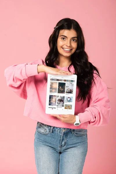 KYIV, UKRAINE - JULY 30, 2019: smiling girl holding digital tablet with pinterest app on screen, isolated on pink — Stock Photo