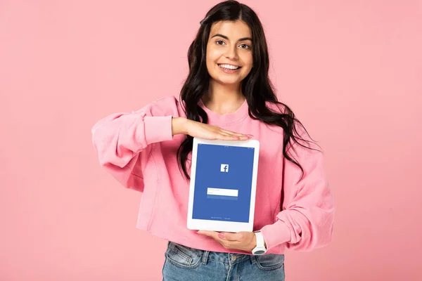 KYIV, UKRAINE - JULY 30, 2019: smiling girl holding digital tablet with facebook app on screen, isolated on pink — Stock Photo