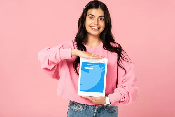 KYIV, UCRANIA - 30 de julio de 2019: niña sonriente sosteniendo la tableta digital con la aplicación de twitter en la pantalla, aislada en rosa - foto de stock