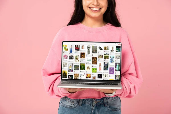 Київ, Україна-30 липня 2019: обрізаний вигляд усміхнена дівчина тримає ноутбук з веб-сайтом Pinterest на екрані, ізольованою на рожевому — стокове фото