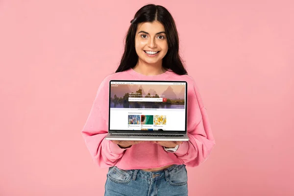 KYIV, UKRAINE - JULY 30, 2019: beautiful smiling girl holding laptop with shutterstock website on screen, isolated on pink — Stock Photo