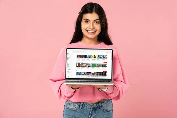 Київ, Україна-30 липня 2019: усміхнена дівчина тримає ноутбук з сайтом YouTube на екрані, ізольованою на рожевому — стокове фото