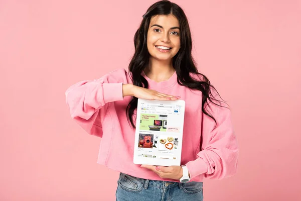 KYIV, UCRANIA - 30 de julio de 2019: niña sonriente sosteniendo la tableta digital con la aplicación ebay en la pantalla, aislada en rosa - foto de stock