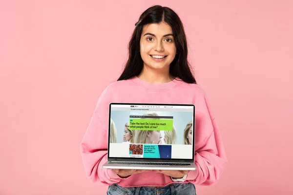 KYIV, UCRÂNIA - JULHO 30, 2019: menina sorridente segurando laptop com site da BBC na tela, isolado em rosa — Fotografia de Stock