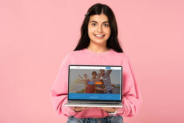 Київ, Україна-30 липня 2019: усміхнена дівчина тримає ноутбук з веб-сайтом каучна на екрані, ізольованою на рожевому — стокове фото