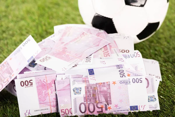 Billetes en euros cerca de pelota de fútbol sobre hierba verde, concepto de apuestas deportivas - foto de stock