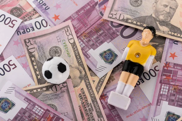 Pelota de fútbol de juguete y jugador de fútbol en billetes de euro y dólar, concepto de apuestas deportivas - foto de stock