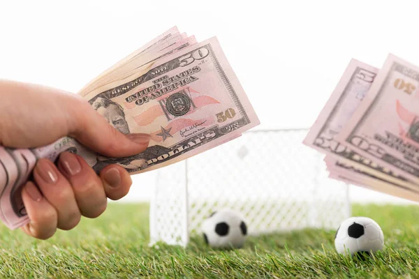 Vista recortada de la mujer sosteniendo billetes de dólar cerca de puertas de fútbol de juguete y pelotas aisladas en blanco, concepto de apuestas deportivas - foto de stock