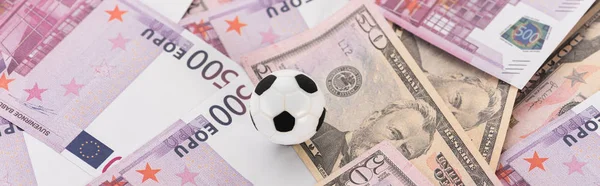 Tiro panorâmico de bola de futebol de brinquedo em notas de dólar e euro, conceito de apostas esportivas — Fotografia de Stock