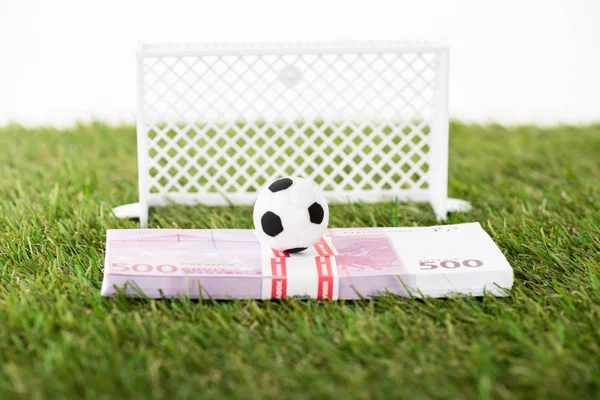 Игрушечный футбольный мяч на банкнотах евро возле миниатюрных футбольных ворот на зеленой траве, изолированной на белой, концепция ставок на спорт — стоковое фото