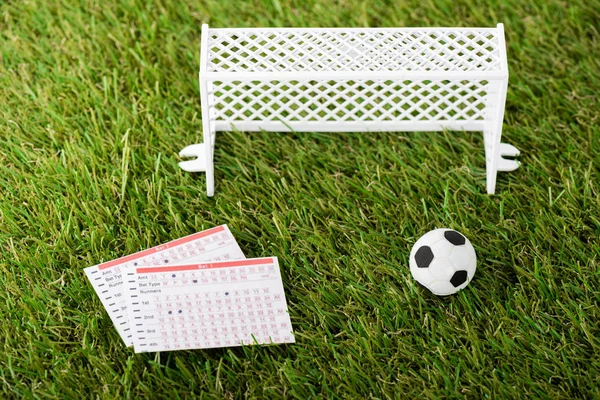 Игрушечный футбольный мяч возле миниатюрных футбольных ворот и списки ставок на зеленую траву, концепция ставок на спорт — стоковое фото