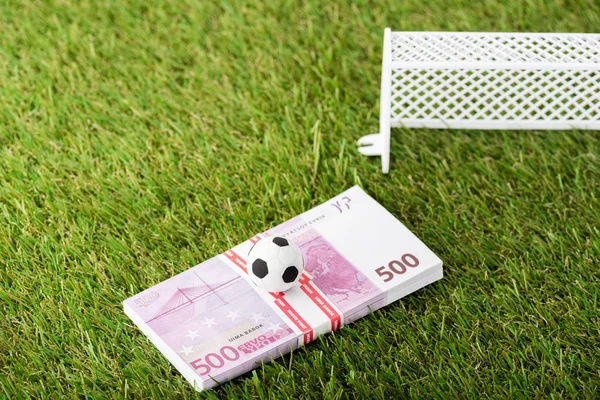 Pelota de fútbol de juguete y billetes en euros cerca de puertas de fútbol en miniatura en hierba verde, concepto de apuestas deportivas - foto de stock