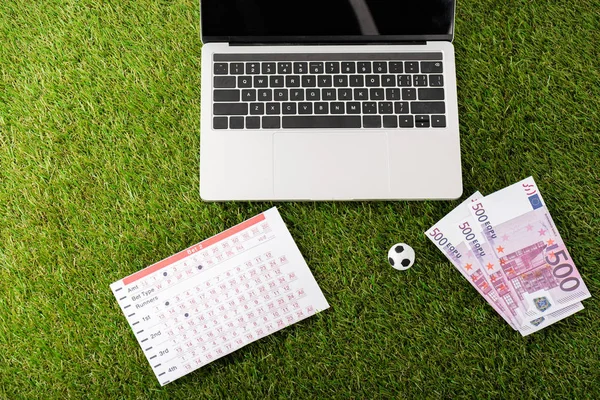 Pelota de fútbol de juguete y lista de apuestas cerca de la computadora portátil en hierba verde, concepto de apuestas deportivas - foto de stock