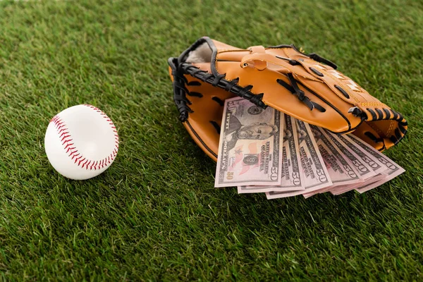 Dollarnoten im Baseballhandschuh in Ballnähe auf grünem Rasen, Sportwetten-Konzept — Stockfoto