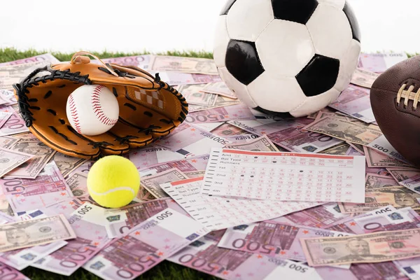 Guante y pelota de béisbol, balones de fútbol, tenis y rugby cerca de las listas de apuestas en euros y billetes de dólar aislados en blanco, concepto de apuestas deportivas - foto de stock