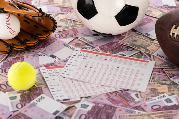 Guante y pelota de béisbol, balones de fútbol, tenis y rugby cerca de las listas de apuestas en billetes de euro y dólar, concepto de apuestas deportivas - foto de stock