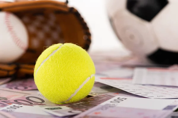 Enfoque selectivo de la pelota de tenis cerca de la pelota de fútbol, el guante de béisbol y la pelota en billetes de dólar y euro aislados en blanco, concepto de apuestas deportivas - foto de stock