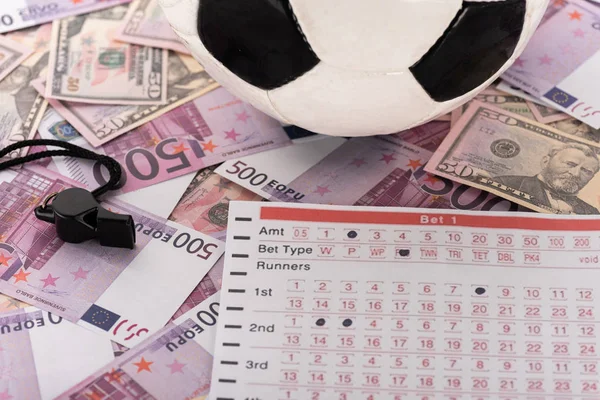Pallone da calcio, fischietto e lista scommesse su banconote in euro e dollari, concetto di scommesse sportive — Foto stock