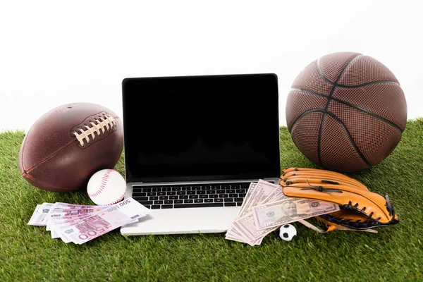 Ноутбук біля спортивних м'ячів, бейсбольна рукавичка, євро і доларові банкноти на зеленій траві ізольовані на білому, концепція спортивних ставок — стокове фото