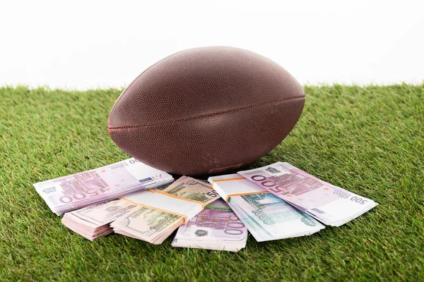 Rugby ball near packs of euro and dollar banknotes on green grass isolated on white, sports betting concept — Stock Photo