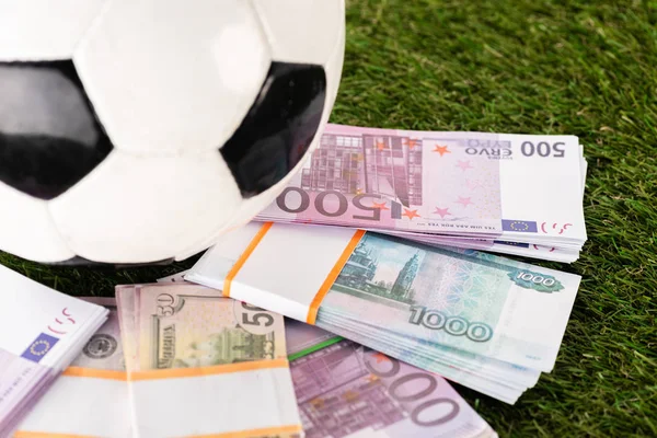 Focalizzazione selettiva di pacchetti di banconote in euro e dollaro vicino al pallone da calcio su erba verde, concetto di scommesse sportive — Foto stock