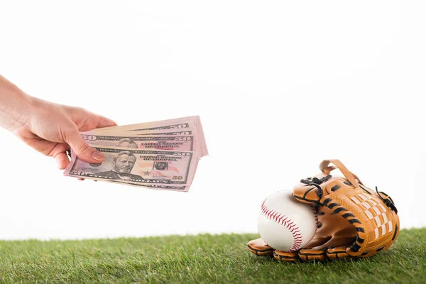 Vue recadrée de la main féminine avec billets en dollars près du gant de baseball et balle sur herbe verte isolé sur blanc, concept de paris sportifs — Photo de stock