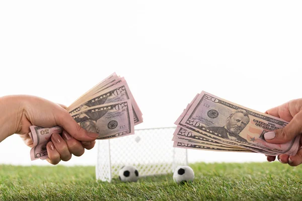 Vista parziale di mani femminili con banconote dollaro vicino palloni da calcio giocattolo e cancelli su erba verde isolato su bianco, concetto di scommesse sportive — Foto stock