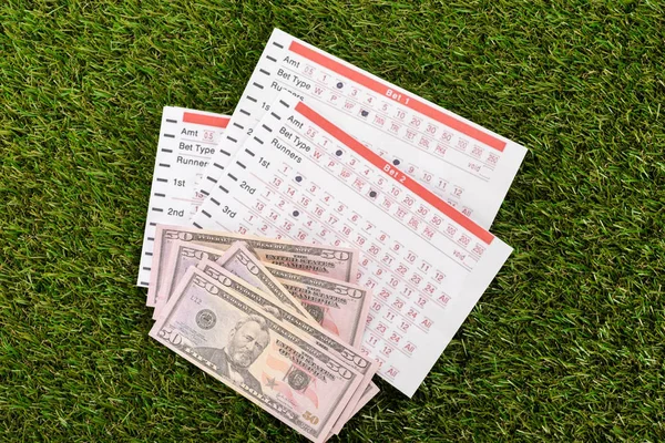 Vista superior de billetes de dólar y listas de apuestas en hierba verde, concepto de apuestas deportivas - foto de stock