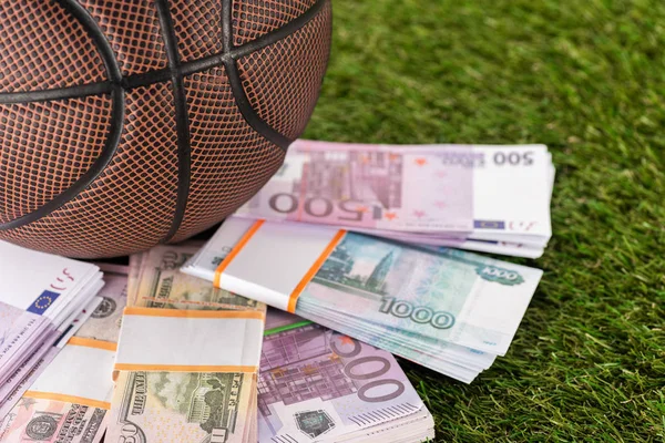 Vista de perto da bola de basquetebol perto do dólar e notas de euro na grama verde, conceito de apostas desportivas — Fotografia de Stock