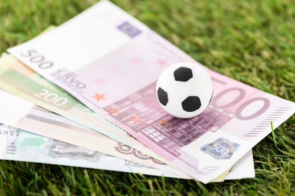 Enfoque selectivo de la pelota de fútbol de juguete y billetes en euros en hierba verde, concepto de apuestas deportivas - foto de stock
