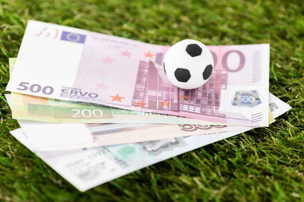 Foco seletivo de bola de futebol de brinquedo e notas de euro em grama verde, conceito de apostas esportivas — Fotografia de Stock