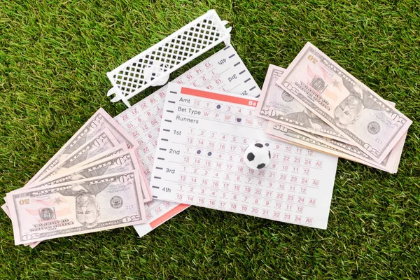 Вид ворот и мяча возле банкнот и списков ставок на зеленую траву, концепция ставок на спорт — стоковое фото