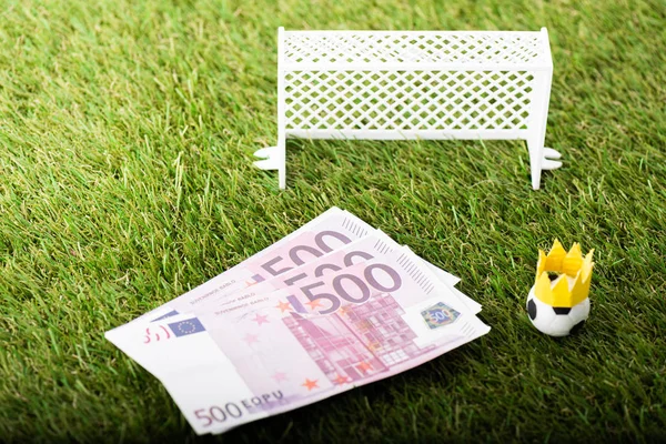 Pallone da calcio giocattolo con corona di carta vicino alle banconote in euro e ai cancelli in miniatura, concetto di scommesse sportive — Foto stock