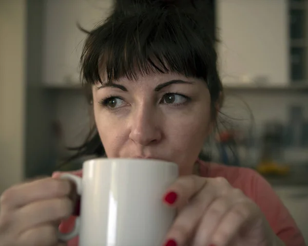 Junge Frau trinkt morgens Kaffee in der Küche, müde Augen mit roten Adern, Nahaufnahme — Stockfoto