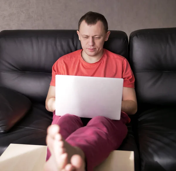 Молодой парень фрилансер, работающий дома на ноутбуке, сидя на диване — стоковое фото