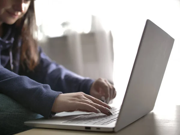 Молодая женщина печатает на ноутбуке, сидя дома на диване — стоковое фото