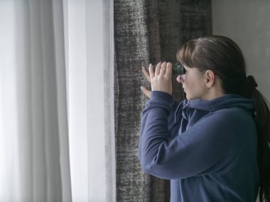 Dürbünle pencereden izleyen genç bir kadın.