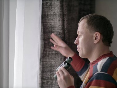 Genç adam dürbünle pencereden dışarı bakıyor, yakın plan.