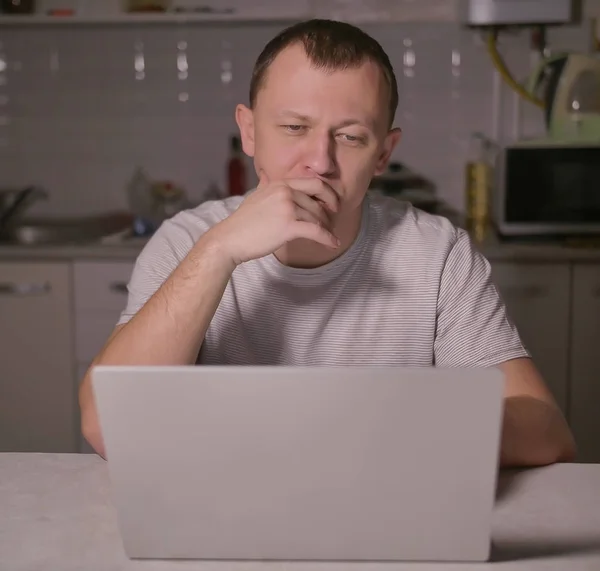 Мужчина сидит вечером на кухне с ноутбуком — стоковое фото