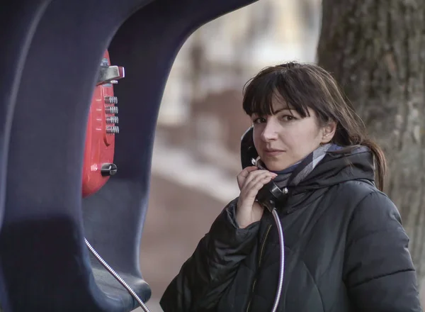 Mladá bruneta žena volá z červené telefonní budky, dívá se přímo do kamery — Stock fotografie