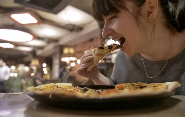 Fiatal nő eszik egy szelet pizzát ül egy kávézóban, közelkép Jogdíjmentes Stock Fotók