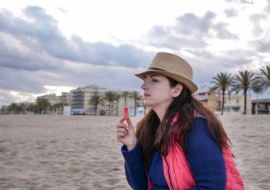 Şapkasevimli kız plajda otururken karpuz yiyor