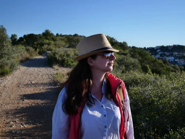 Brunette touristique dans un chapeau et des lunettes de soleil va le long du chemin sur la colline — Photo