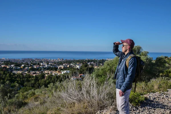 Le voyageur en lunettes de soleil et avec un sac à dos derrière le dos, regarde la zone debout sur une colline, copier l'espace — Photo