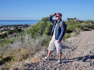 Arkasında sırt çantası olan gezgin adam, bir tepede duran mahalleyi inceliyor, uzayı kopyalıyor.