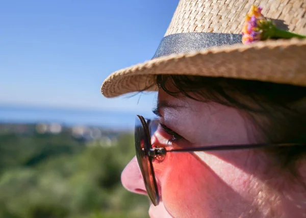 Jolie fille brune en lunettes de soleil et un chapeau avec une fleur regarde ailleurs, gros plan — Photo