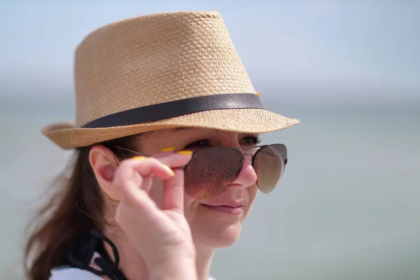 Portrait de jolie fille en lunettes de soleil et un chapeau, tenant des lunettes avec la main, gros plan — Photo